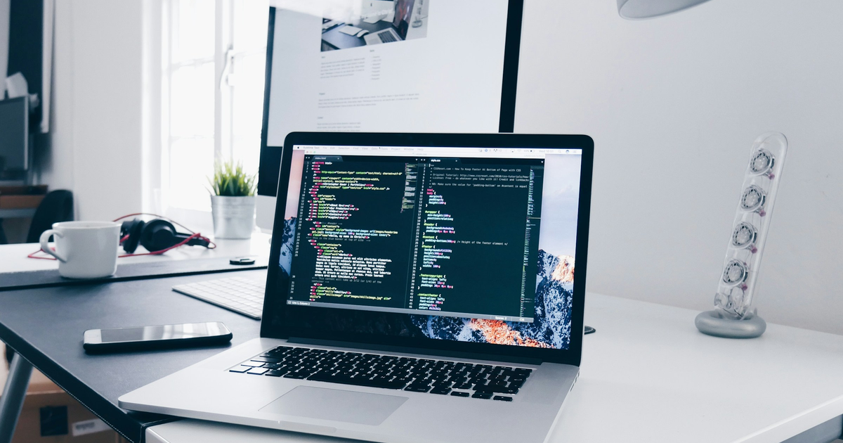 Silver laptop showing a dark code editor on a white desk.