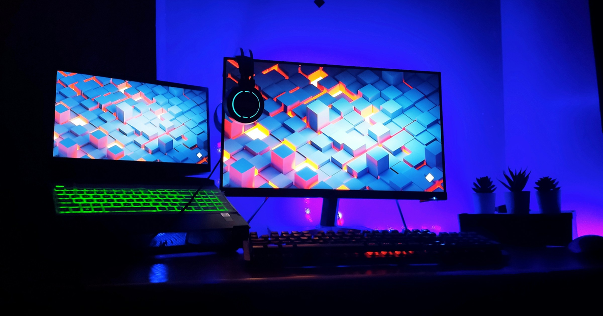 Two monitors with a matching geometric wallpaper under blue light.
