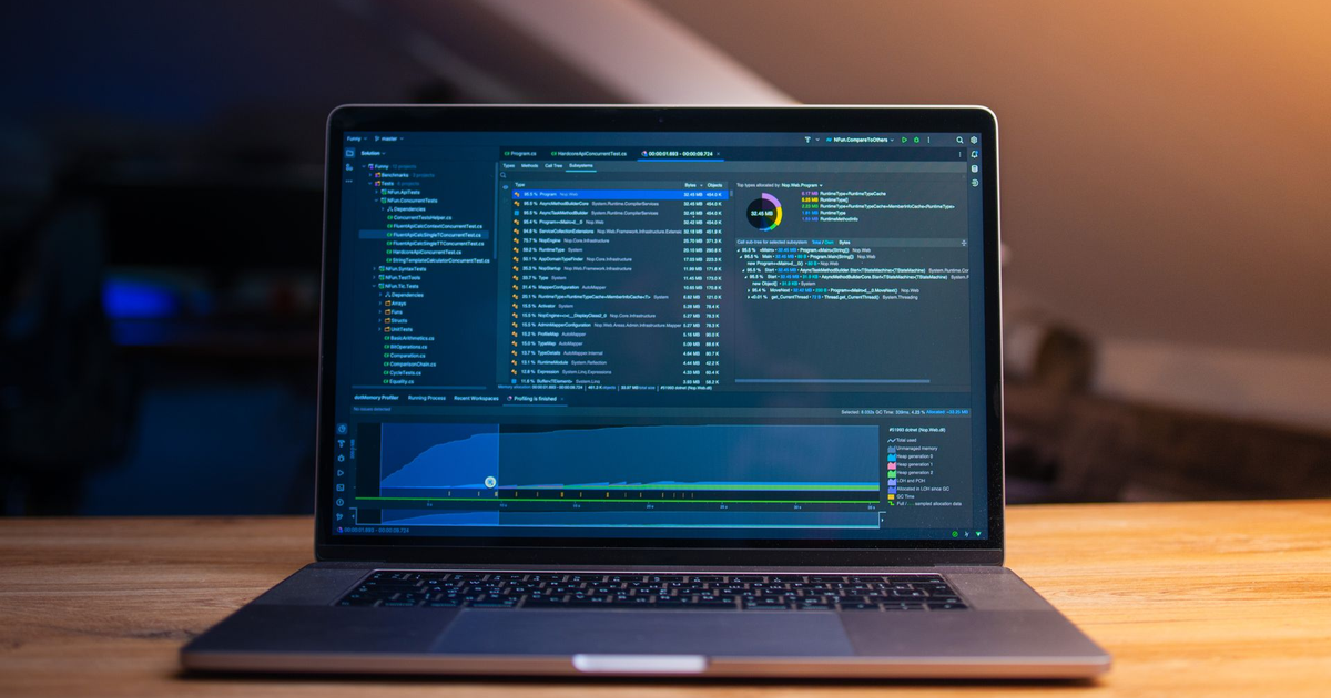 Laptop on a wooden desk showing code in a dark editor, lit by warm window light.