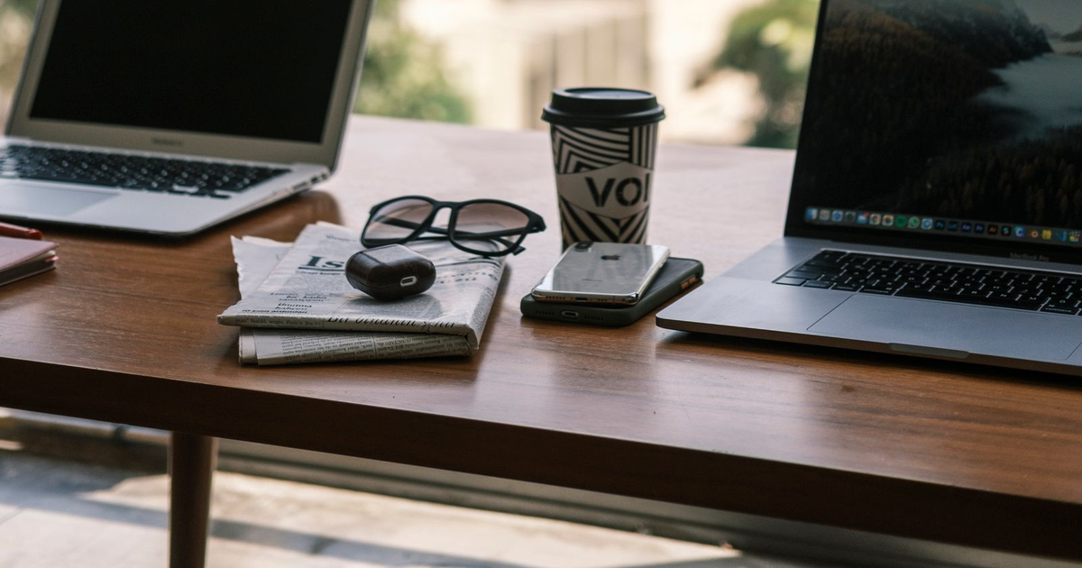 Two laptops on a wood table with coffee, glasses, and a phone.