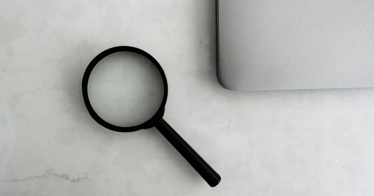 Black magnifying glass beside a closed silver laptop.