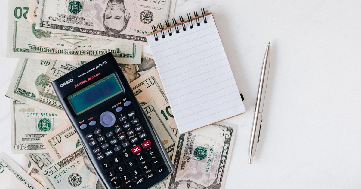 Calculator, notepad, and US dollar bills on a white desk.