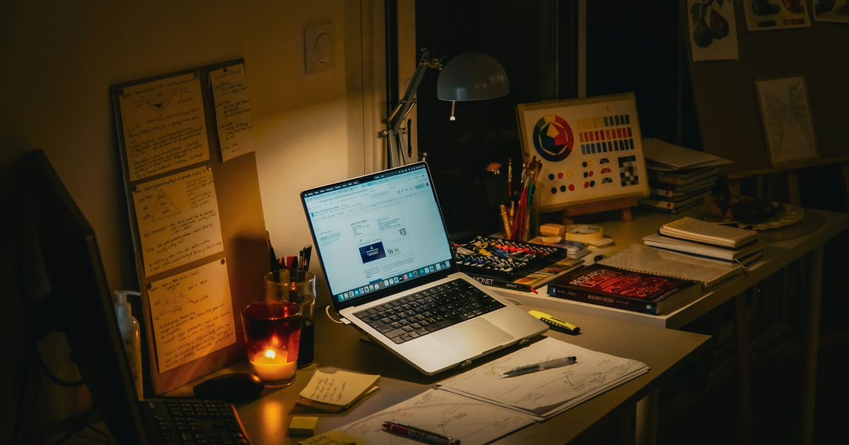 Lamp-lit desk with a laptop, notes, and a research book.