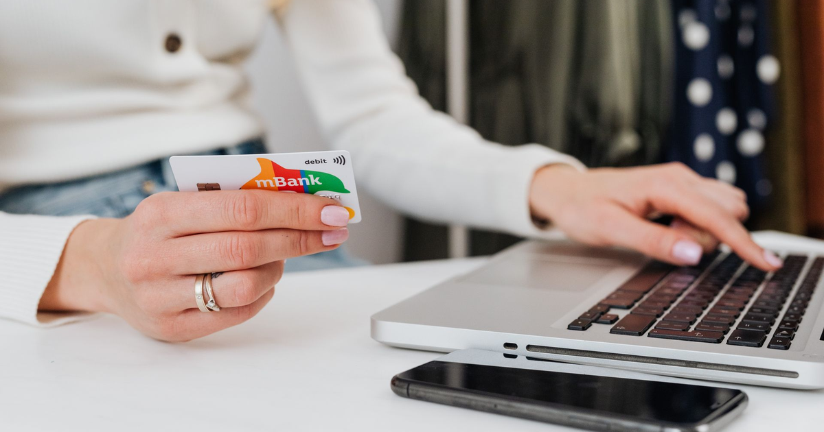 Person holding a bank card in one hand while typing on a laptop to pay online.
