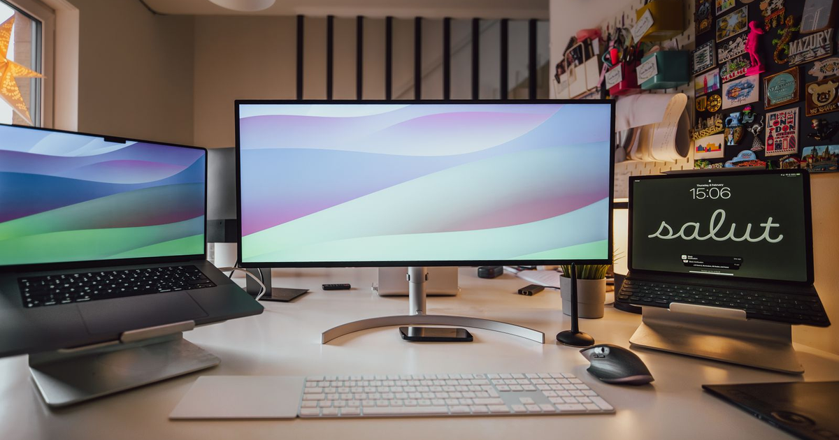 Laptop, ultrawide monitor, and tablet lined up on a white desk.